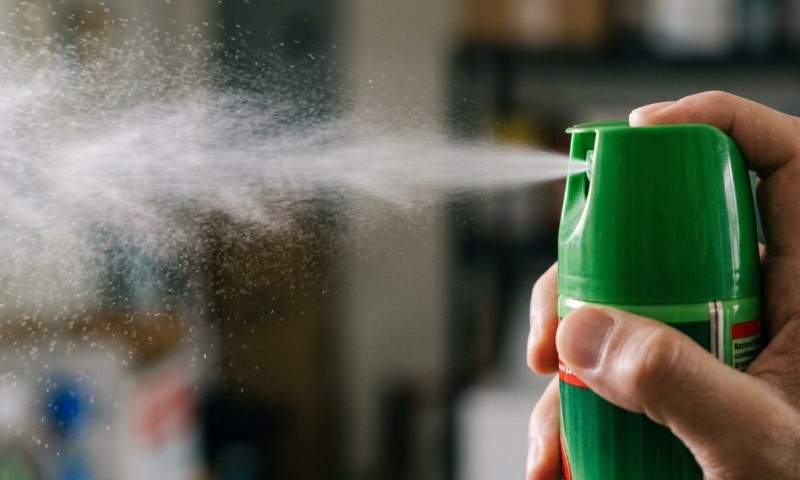 A hand presses a green aerosol spray can